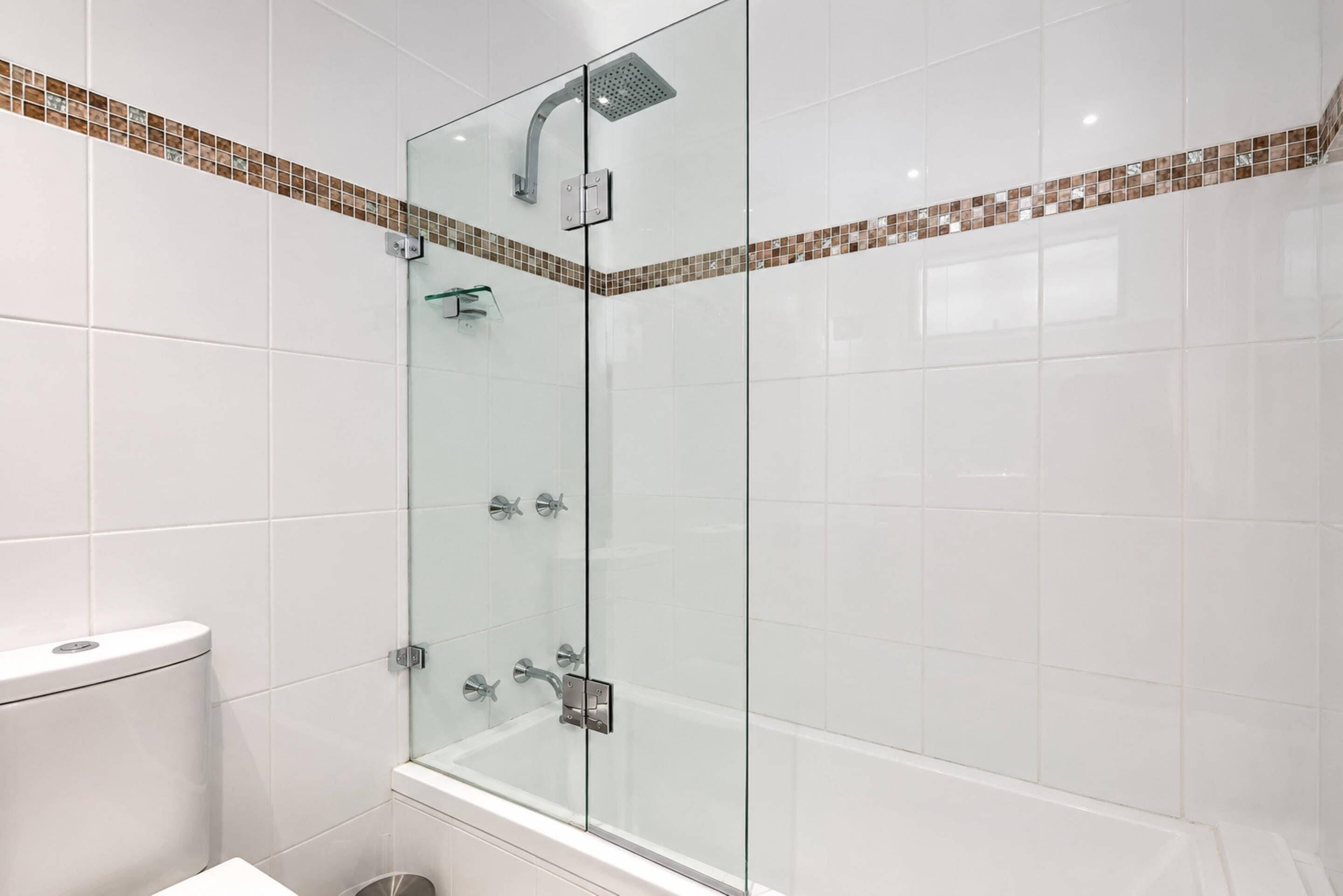A glass-enclosed shower with a handheld showerhead and a wall-mounted faucet.