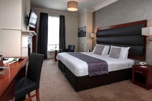 A hotel room with a bed, a desk, a chair, a TV, and a window with curtains. - Lion Hotel (Worksop)