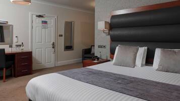 A hotel room with a bed, a desk, a chair, a dresser, a nightstand, a lamp, a mirror, and a door.