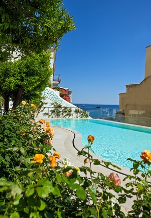 Una piscina con vista despejada al mar, rodeada de exuberante vegetación y un edificio de fachada blanca.
