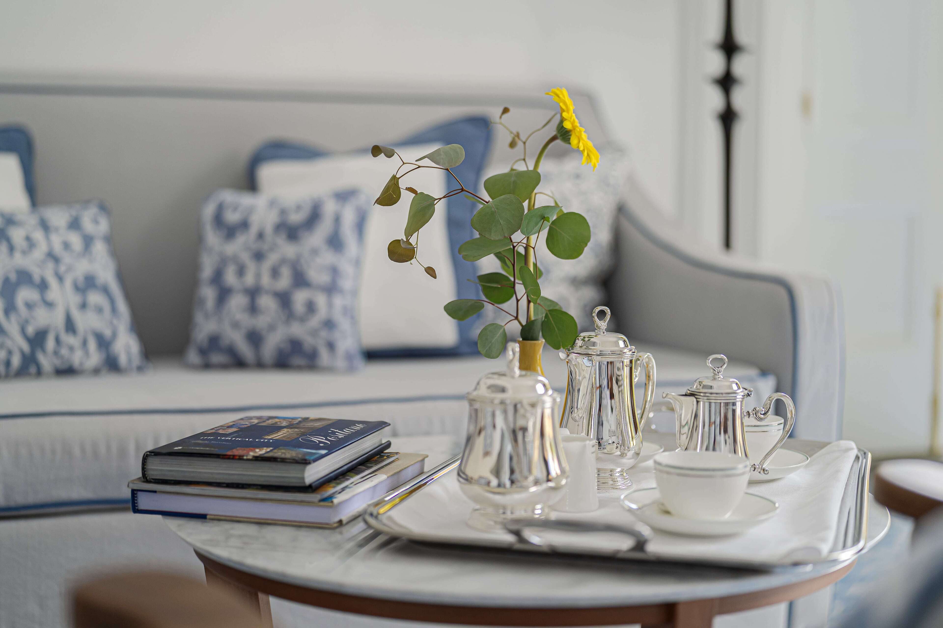A tray with tea set and books on a table in a room with a sofa and patterned cushions.