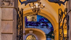 Una entrada ornamentada con arco, con una araña, que conduce a un espacio con vistas a un balcón y plantas en macetas.