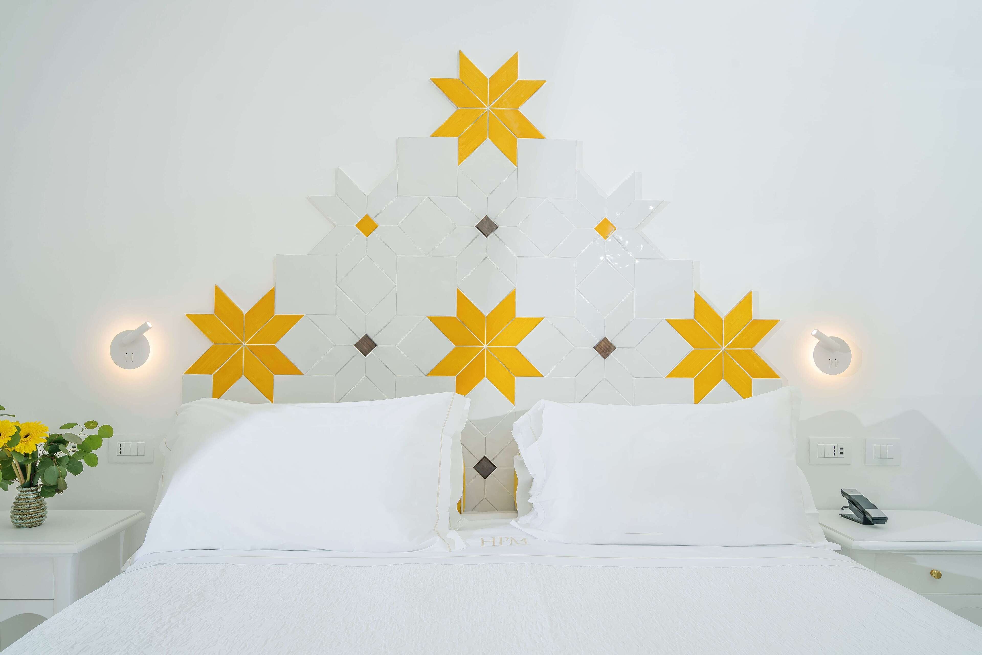 A hotel room with a bed, white bedding, a nightstand with a phone, and decorative wall panels.