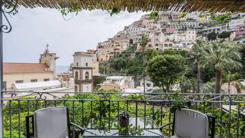 A balcony with two chairs and a table, overlooking a hillside with buildings and a church.
