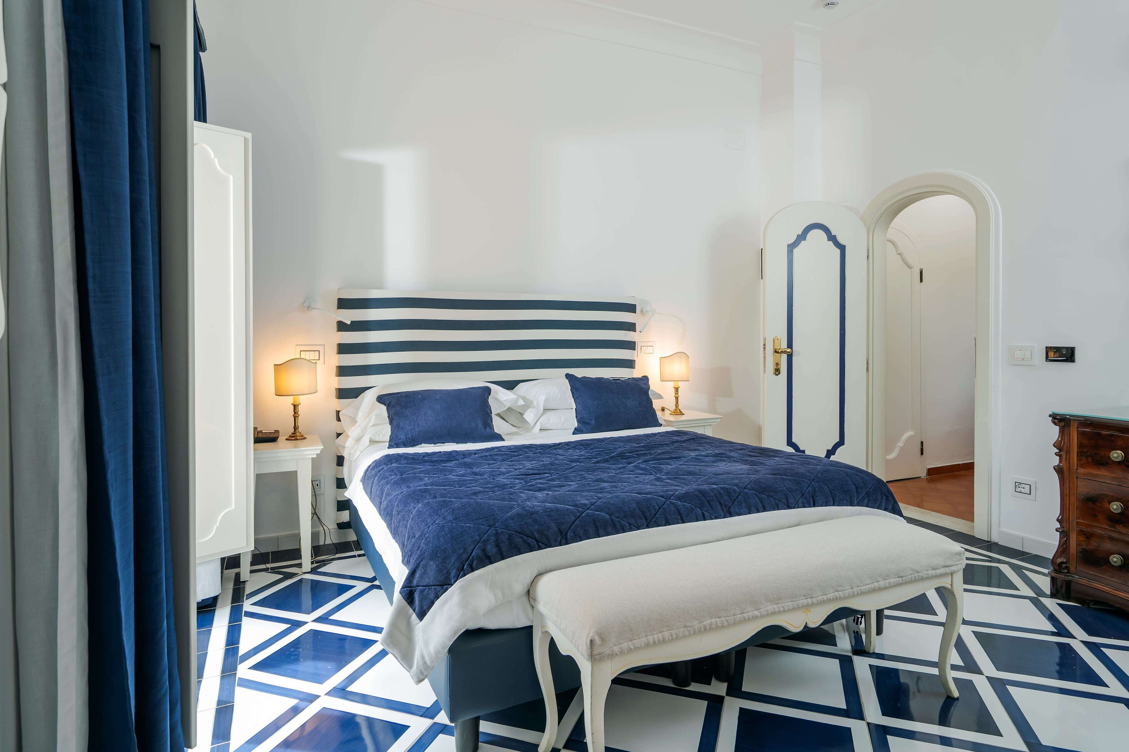 Ein Schlafzimmer mit einem großen Bett, Nachttischen mit Lampen, einer Bank und einem Kleiderschrank.