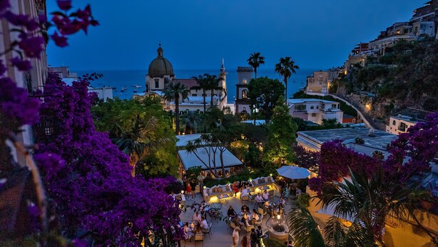 Un pueblo costero con una cúpula de iglesia destacada, un patio con asientos y vistas al mar.