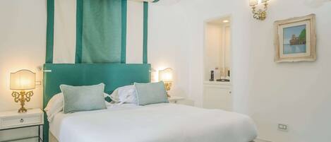 A neatly made bed with white linens and two pillows, a teal accent headboard, and a nightstand with a lamp.