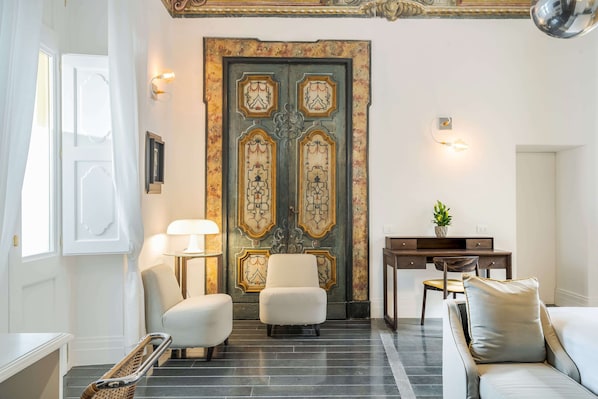 A room with a large ornate door, two armchairs, a sofa, a desk with a chair, and a lamp. - Palazzo Murat Hotel (Positano)