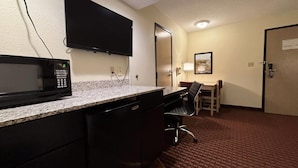 Habitación de hotel con kitchenette, un televisor de pantalla plana en la pared, un escritorio con una silla y una puerta.
