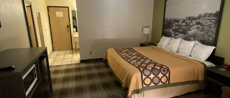 A hotel room with a bed, a desk, a chair, a nightstand, a lamp, and a painting on the wall.
