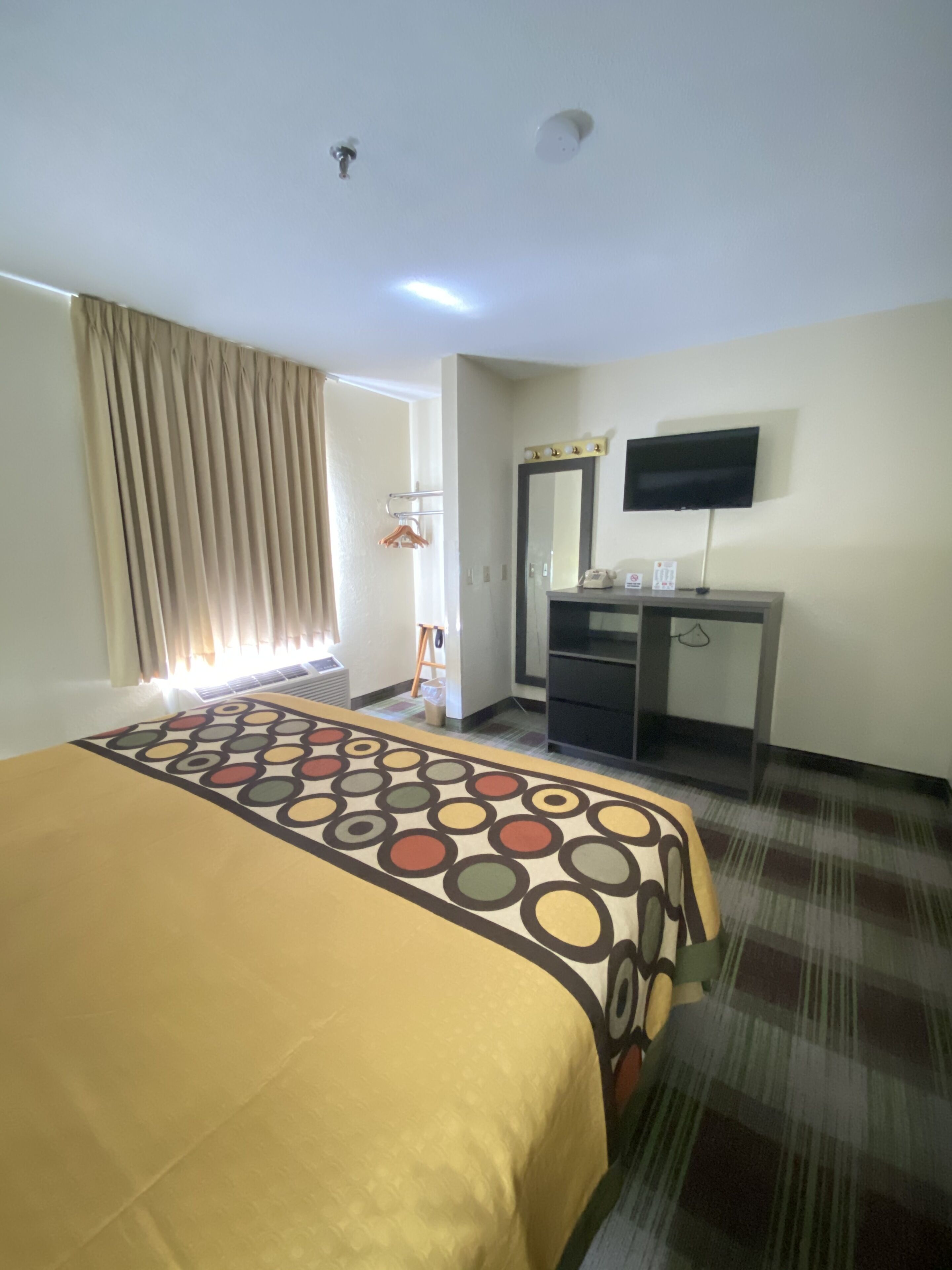 Habitació d'hotel amb un llit, una taula de treball, televisió i una finestra amb cortines.