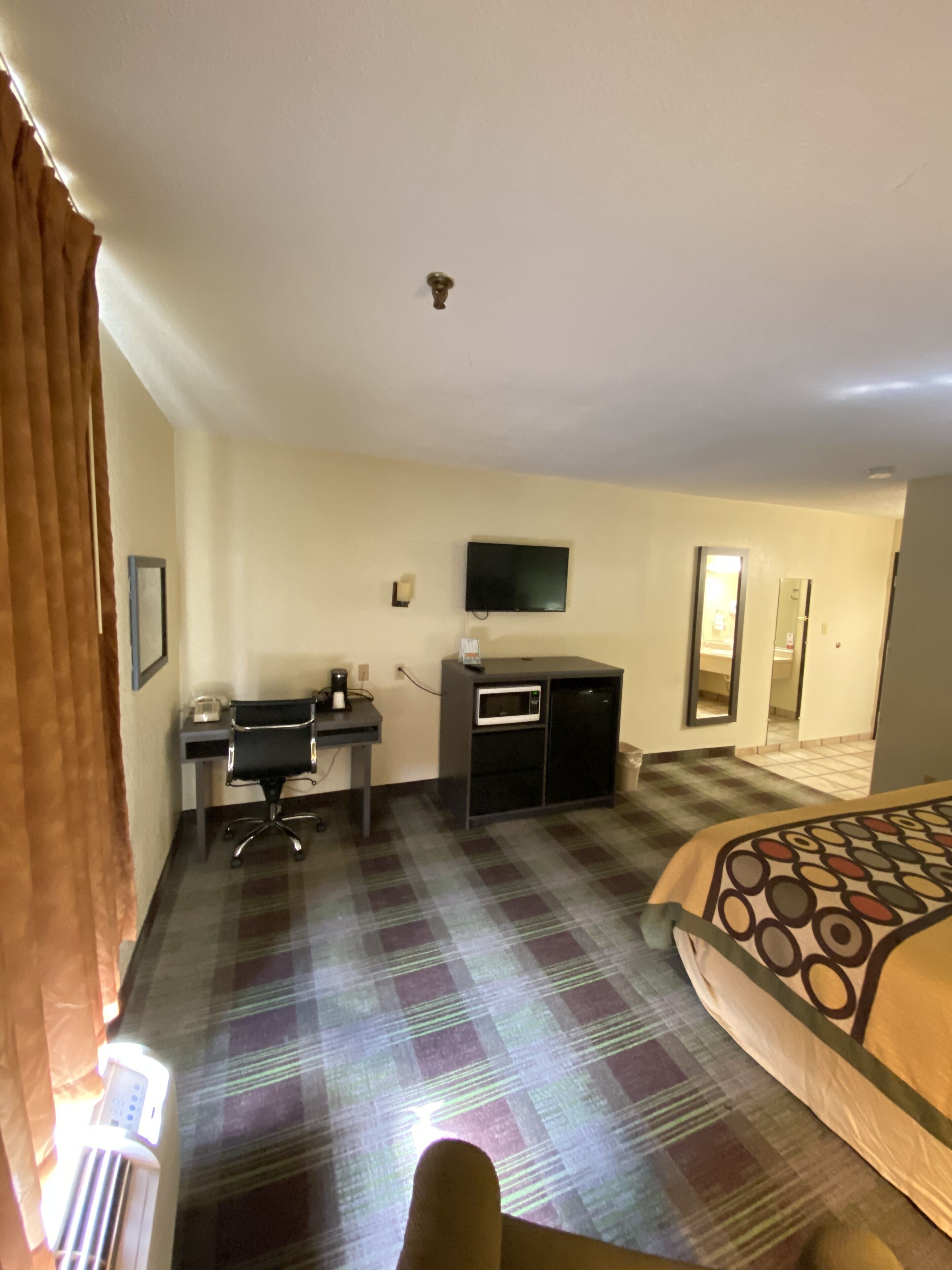 Une chambre d’hôtel comprenant un lit, un bureau avec une chaise, une télévision, un four à micro-ondes et une petite table.