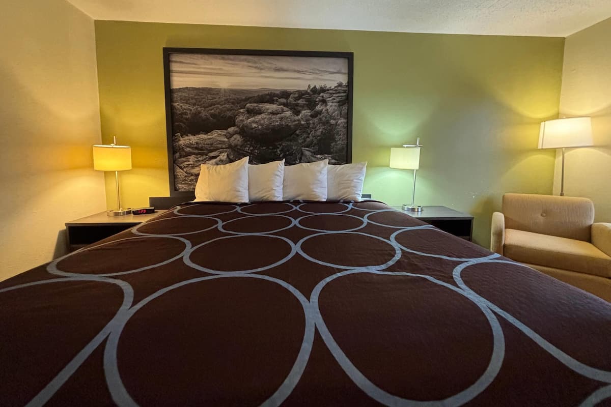 A hotel room with a large bed, two bedside tables, a chair, and a wall-mounted lamp.