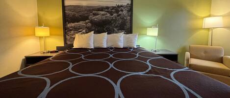 Una habitación de hotel con una cama grande, dos mesitas de noche, una silla y una lámpara de pared.