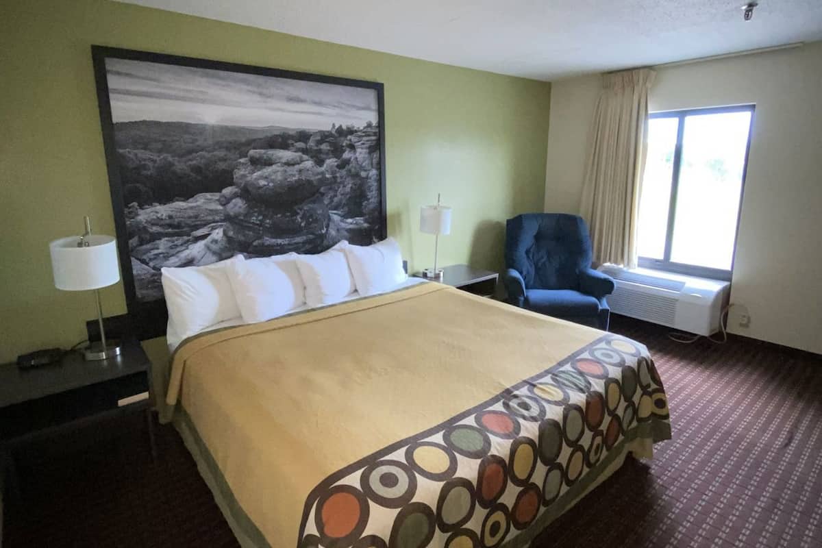 A hotel room with a bed, a chair, a window, and a painting on the wall.