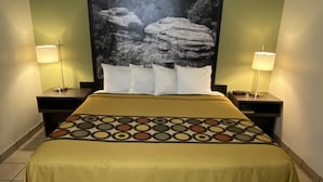 Habitación de hotel con cama, dos mesitas de noche, dos lámparas, un cuadro grande en la pared y una colcha estampada.