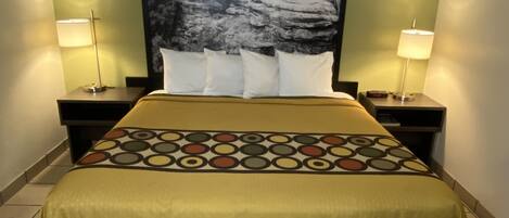 Una camera d'albergo con un letto, due comodini, due lampade, un quadro di grandi dimensioni appeso al muro e una coperta con motivo.