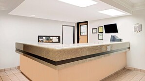 Zona de recepción con mostrador, una puerta, televisor montado y certificados enmarcados en la pared.