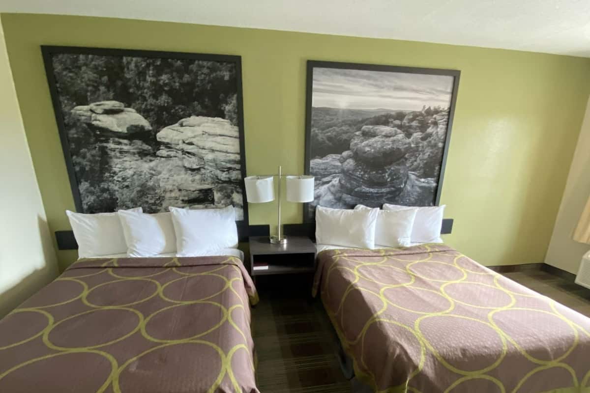 A hotel room with two beds, a nightstand, and two wall-mounted lamps.