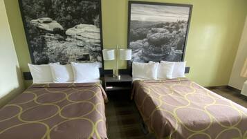 Ein Hotelzimmer mit zwei Betten, jeweils mit einem gemusterten Überwurf, einem Nachttisch mit einer Lampe sowie zwei großen gerahmten Bildern an der Wand.