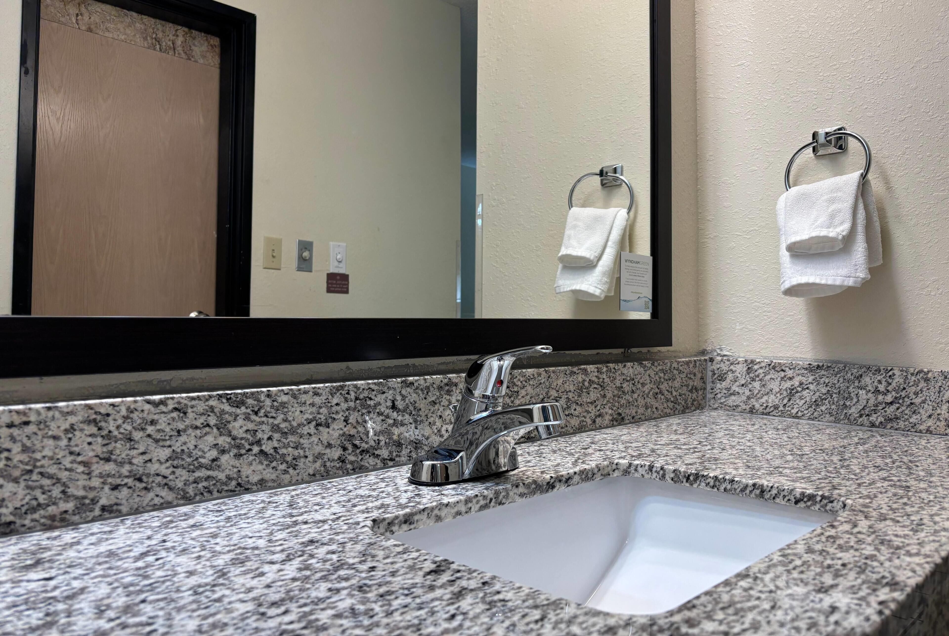 A bathroom with a granite countertop, a sink, a mirror, and two towels hanging on towel rings.