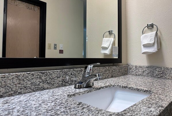 Une salle de bain avec un comptoir en granit, un lavabo, un miroir et deux serviettes suspendues à des porte-serviettes.