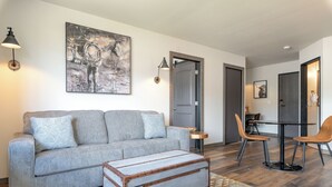 A living room with a grey sofa, a patterned rug, a wooden chest, and a dining area with chairs and a table. - MTN Lodge Ridgway (Ridgway)