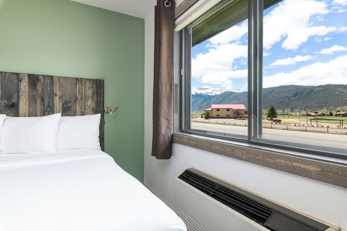 A hotel room with a large bed, a view of mountains, and a window with curtains.
