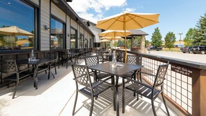 An outdoor patio with tables and chairs, large umbrellas, and a view of the parking lot and trees. - MTN Lodge Ridgway (Ridgway)