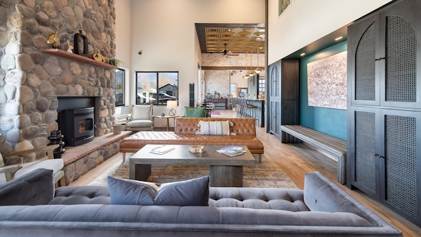 A spacious living area with a stone fireplace, leather sofa, and a dining area with a high ceiling and wooden beams. - MTN Lodge Ridgway (Ridgway)