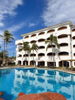 A hotel with a pool, palm trees, and a clear blue sky.