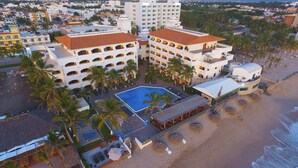 A hotel with multiple floors, a swimming pool, and a beach area with umbrellas.