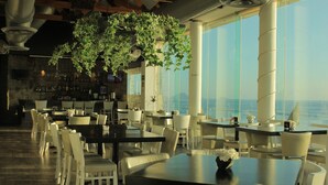 A restaurant with tables and chairs, a bar area, and a view of the sea.