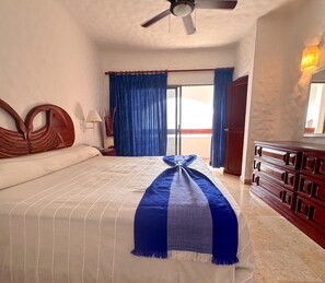 A hotel room with a large bed, a ceiling fan, a wooden dresser, and a view of the outside through a sliding glass door.