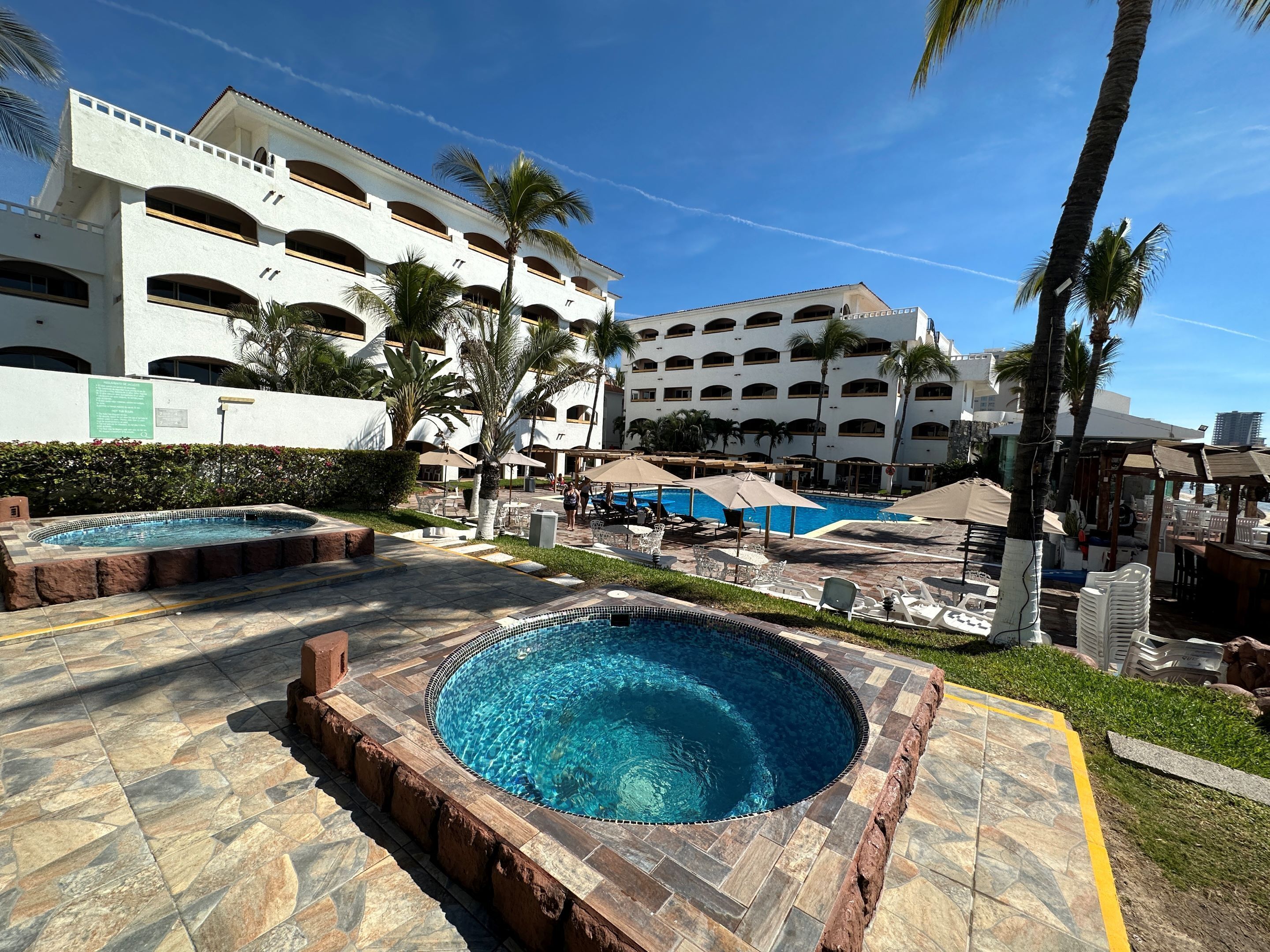 Zona de piscina de hotel con jacuzzi, sillas de descanso y sombrillas.