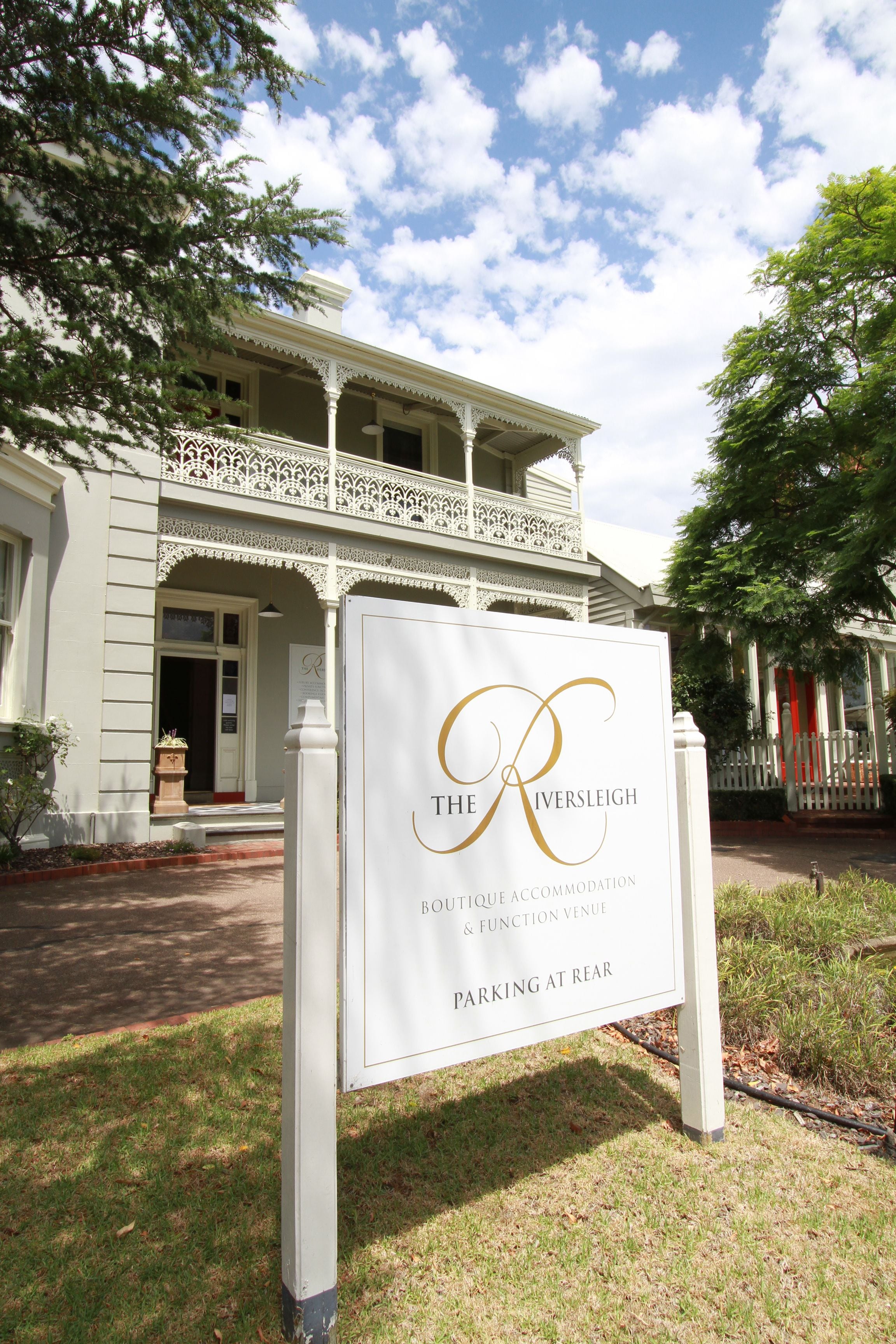 Une enseigne indiquant « The Riversleigh Boutique Accommodation & Function Venue », avec un bâtiment blanc en arrière-plan.