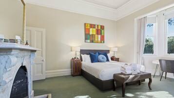 A hotel room with a bed, bedside lamps, a fireplace, a desk, and a window with a view.