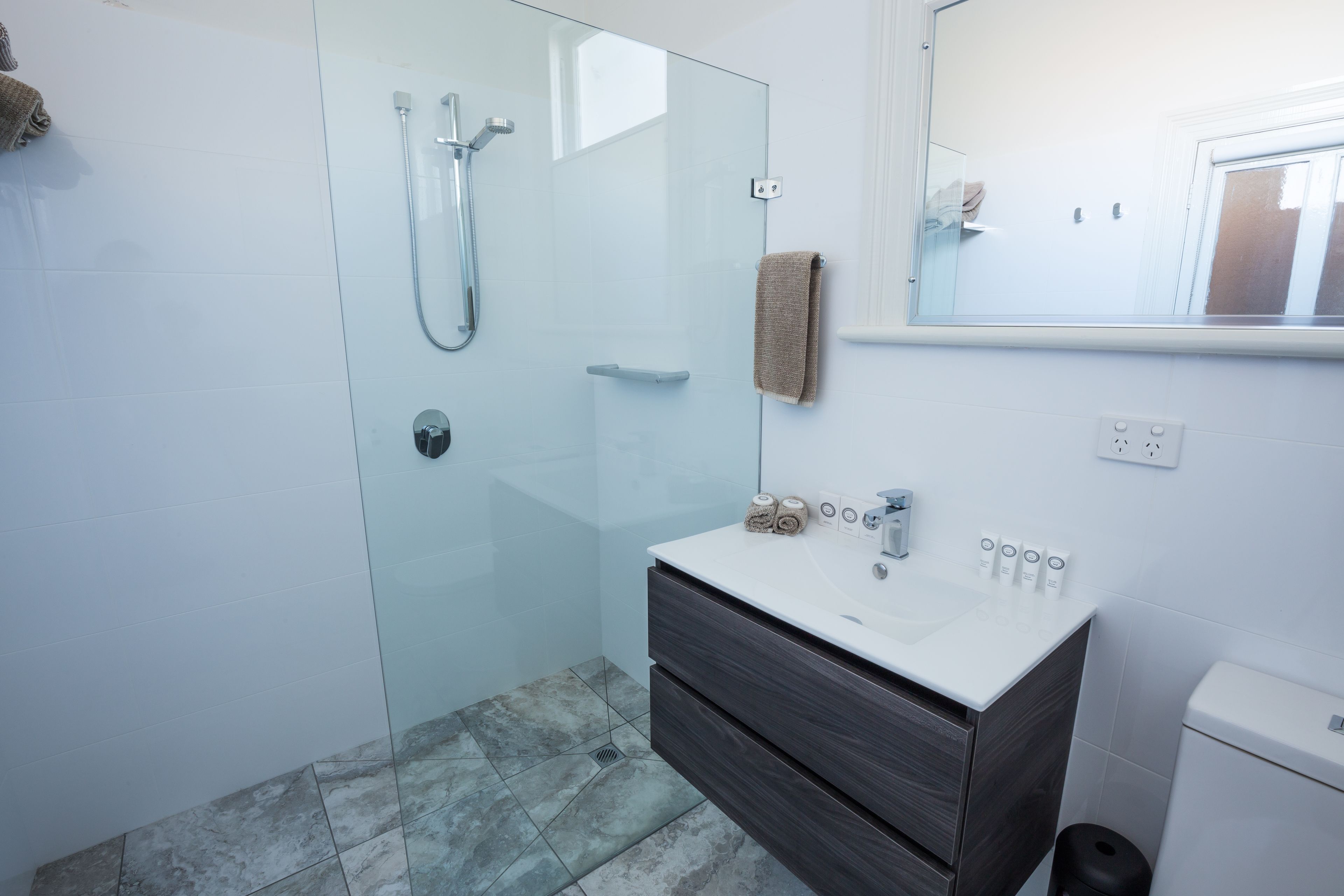A modern bathroom with a glass-enclosed shower, a white sink with dark wooden vanity, and a mirror above the sink.