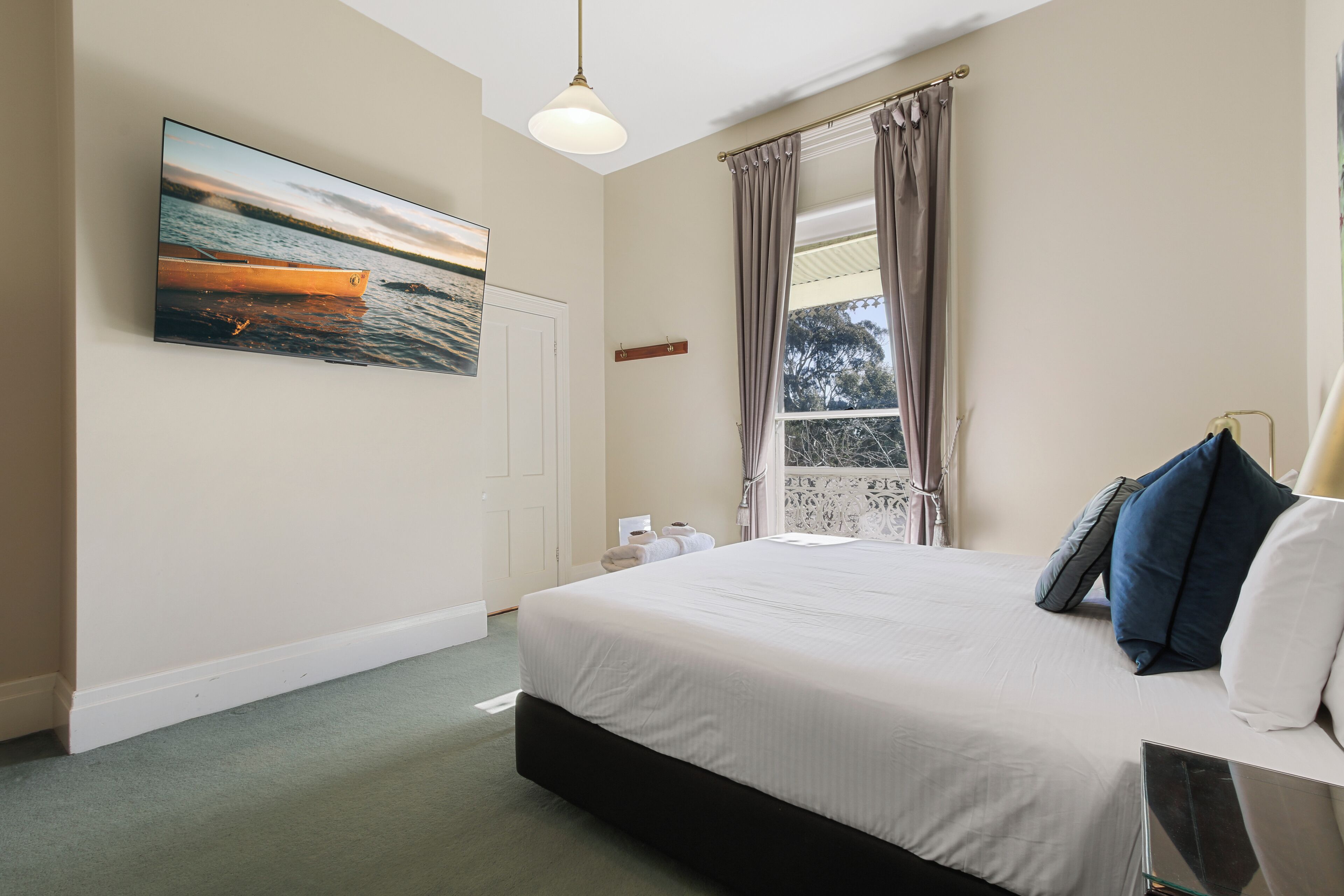 Une chambre avec un grand lit, une fenêtre avec des rideaux, un tableau représentant un bateau accroché au mur et un luminaire suspendu.