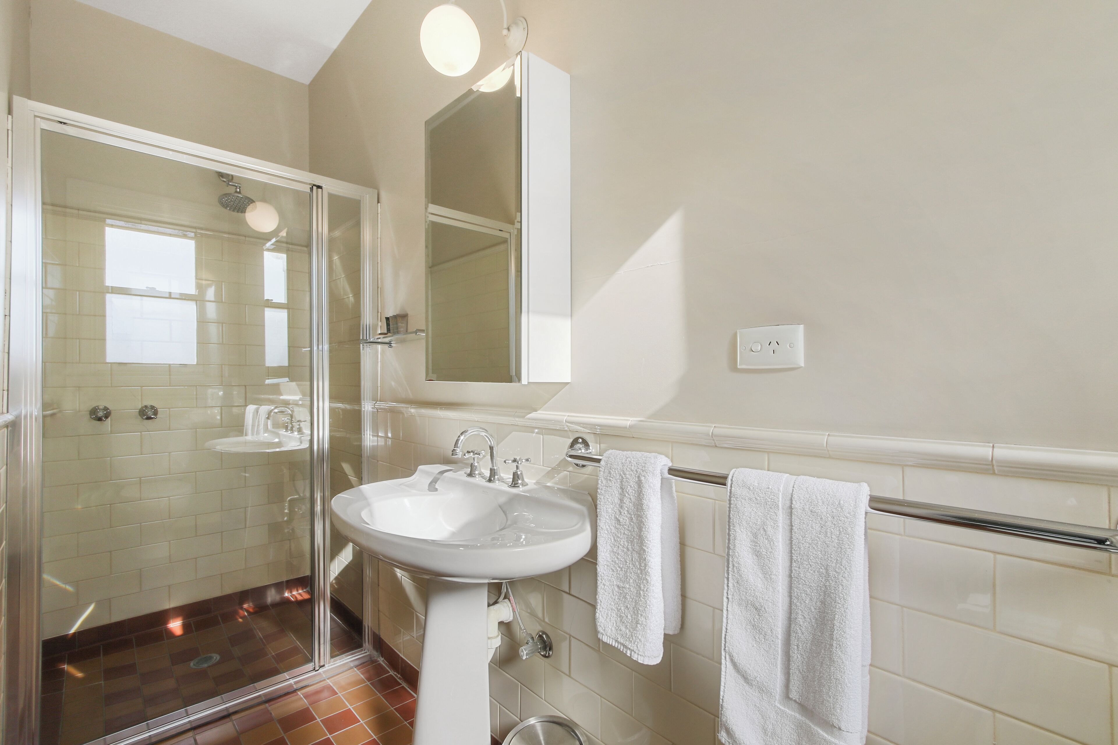 Une salle de bain avec une douche à parois de verre, un lavabo blanc et un miroir au-dessus du lavabo.