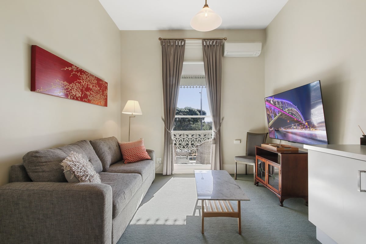 Un salon moderne avec un canapé, une table basse, un téléviseur et un balcon agrémenté de rideaux.