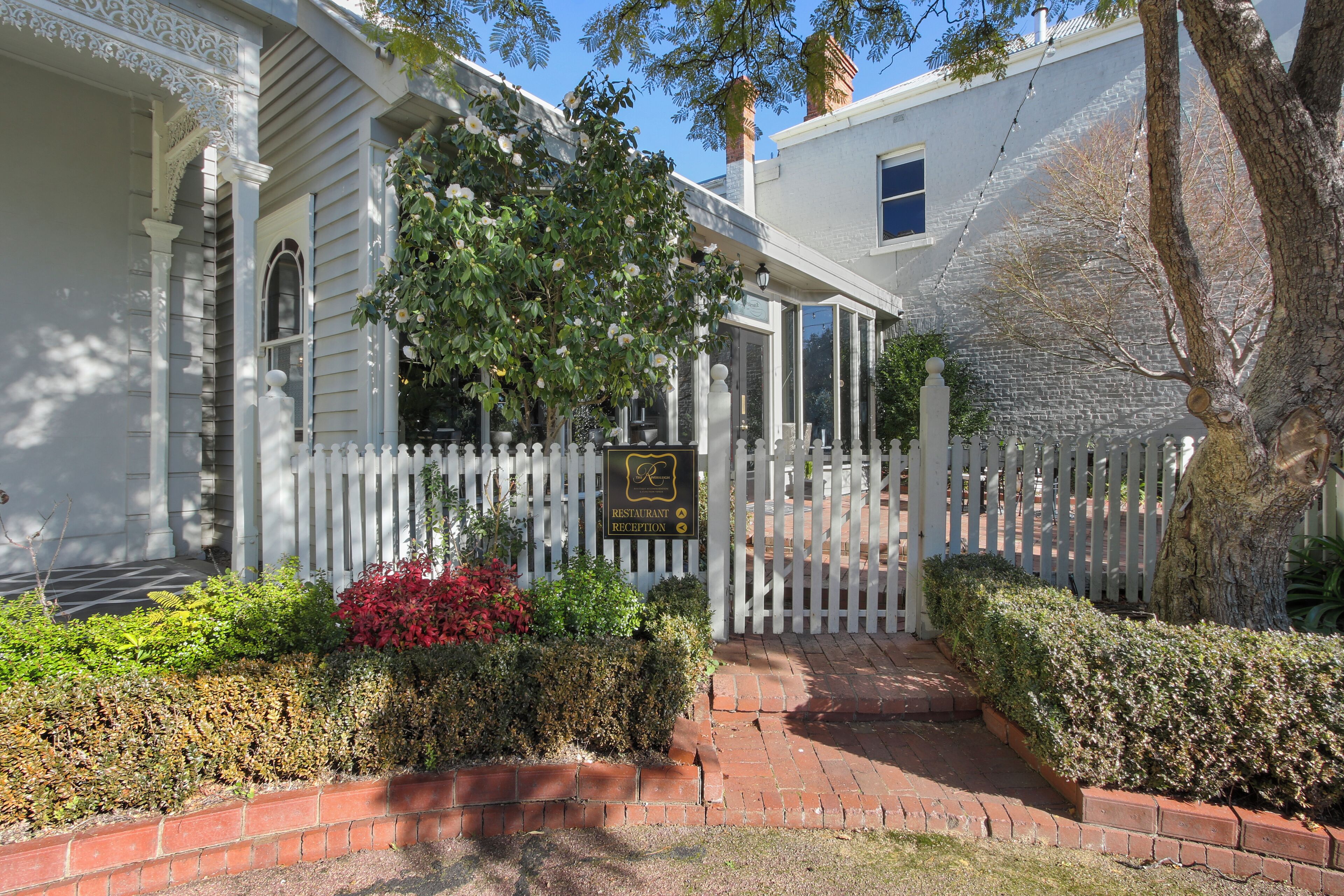 A white building with a reception sign, a white picket fence, and a brick pathway leading to the entrance.