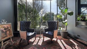 Una habitación con dos sillones tapizados, un alfombra estampado, un cuadro enmarcado y una planta en maceta.