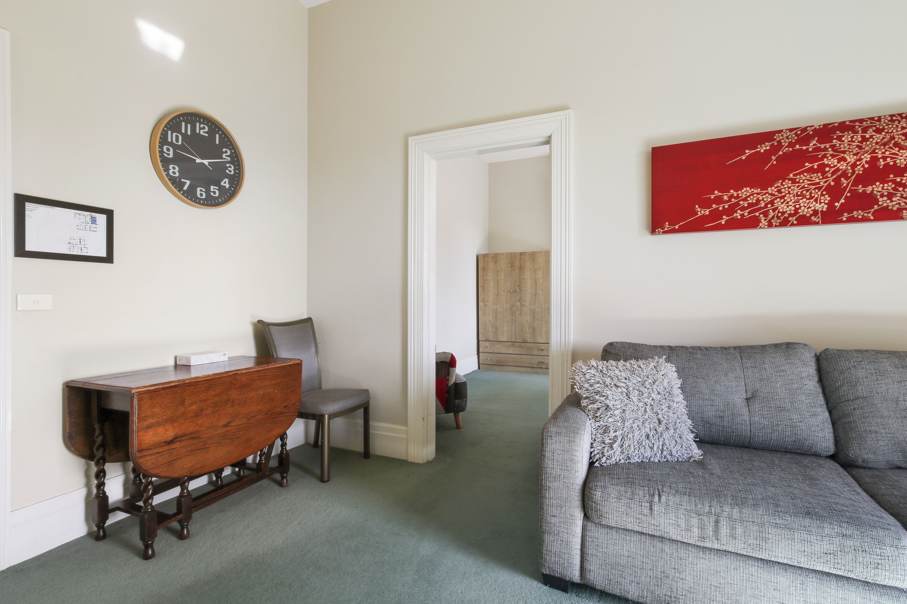 A living room with a wooden coffee table, a grey sofa, a red artwork, and a clock on the wall.