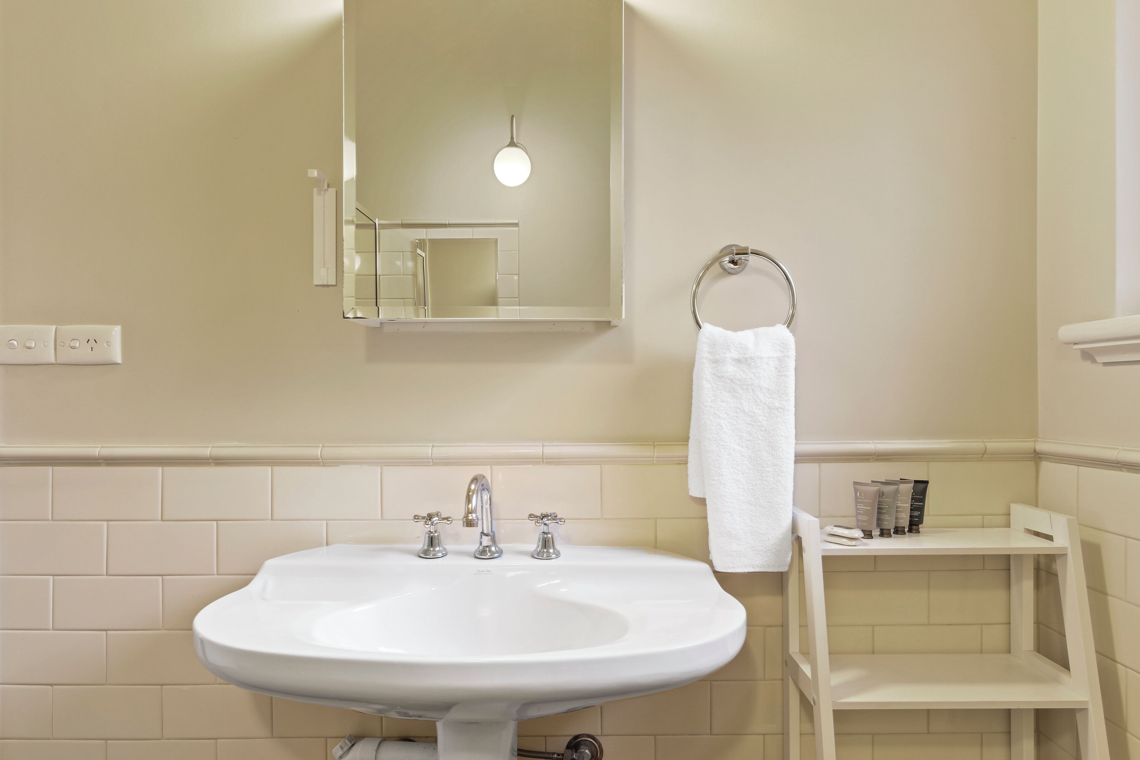 Ein Badezimmer mit einem weißen Waschbecken, einem Spiegel, einem Handtuchhalter und einem Ablagebereich für Toilettenartikel.
