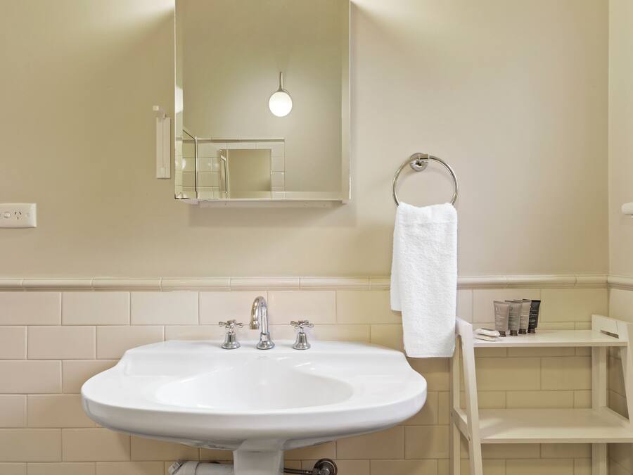 Ein Badezimmer mit einem weißen Waschbecken, einem Spiegel, einem Handtuchhalter und einem Ablagebereich für Toilettenartikel.