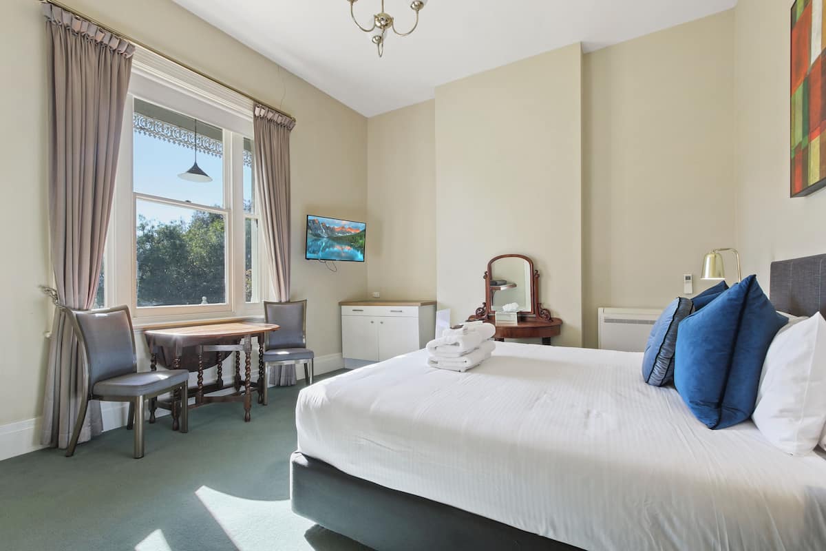Une chambre d’hôtel avec un grand lit, un bureau, une chaise, une télévision et une fenêtre avec des rideaux.