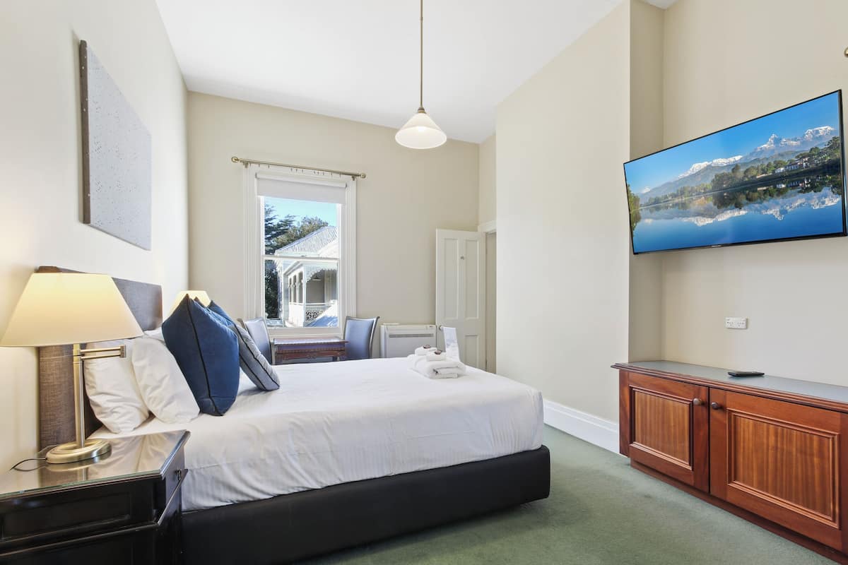 Une chambre d’hôtel équipée d’un lit, d’une télévision, d’un bureau et d’une fenêtre donnant sur une vue sur la montagne.