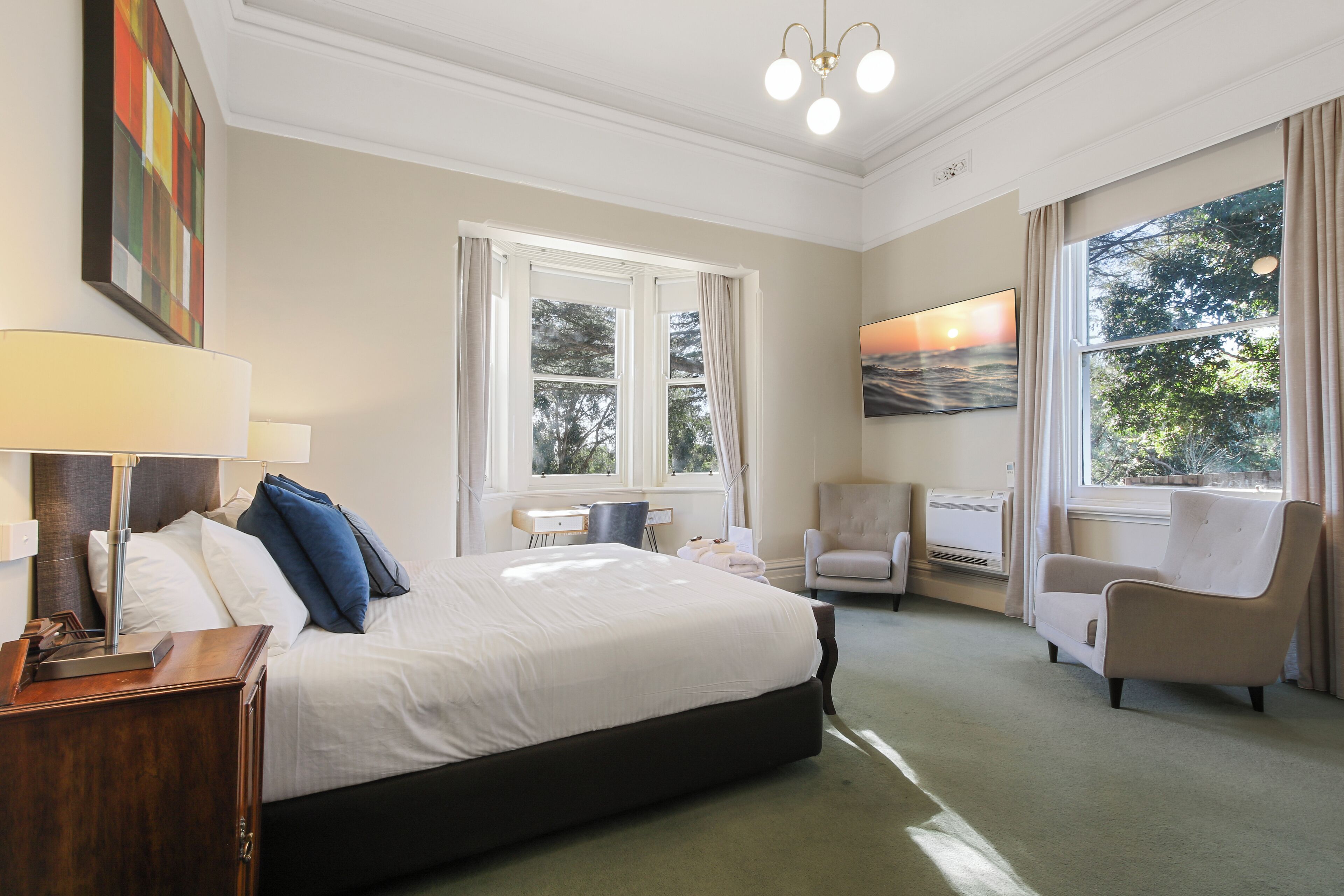 Une chambre d’hôtel avec un grand lit, deux chaises, un bureau et un tableau au mur.