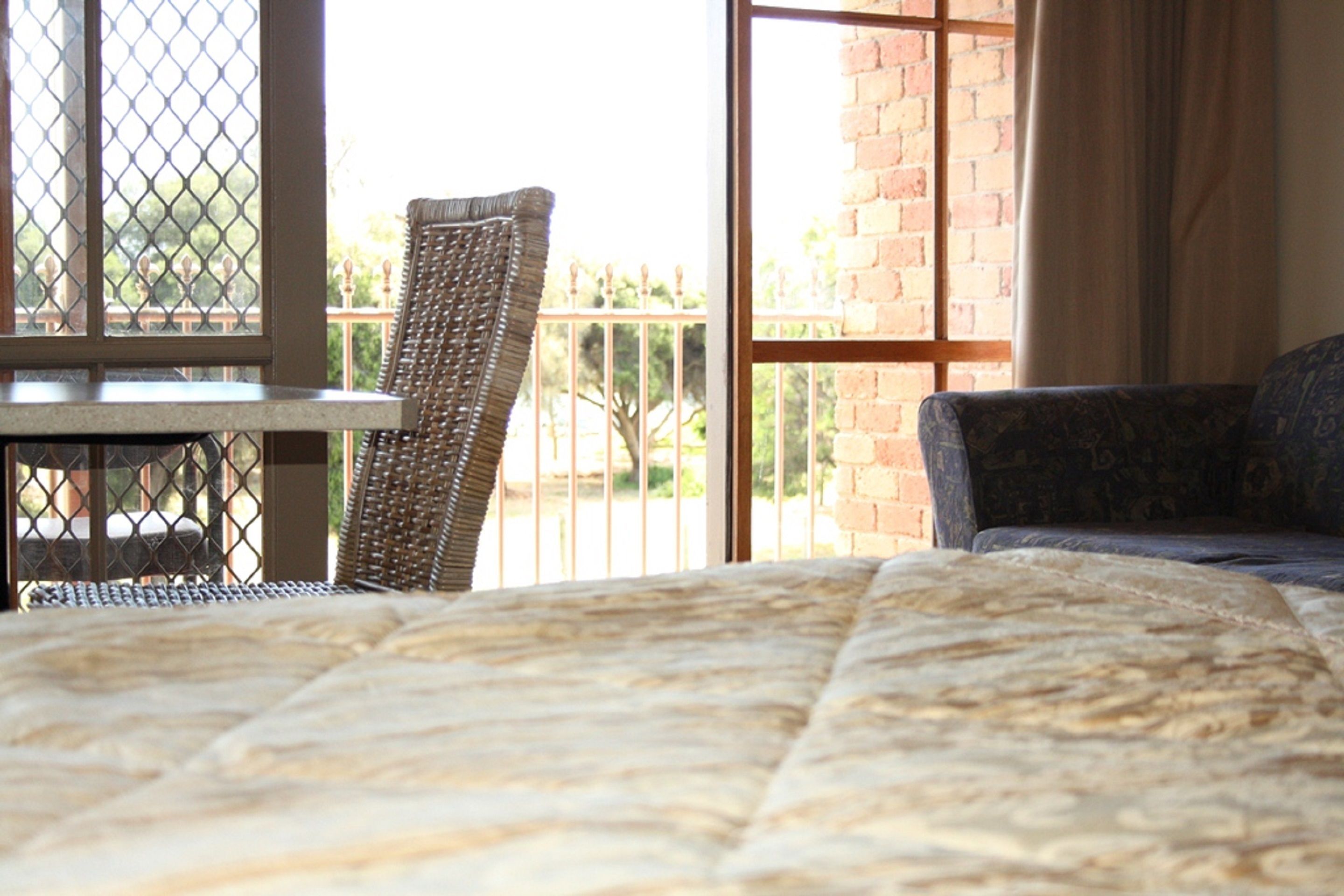 Una habitación con cama, una silla y una mesa cerca de una ventana que da a una pared de ladrillo y follaje.